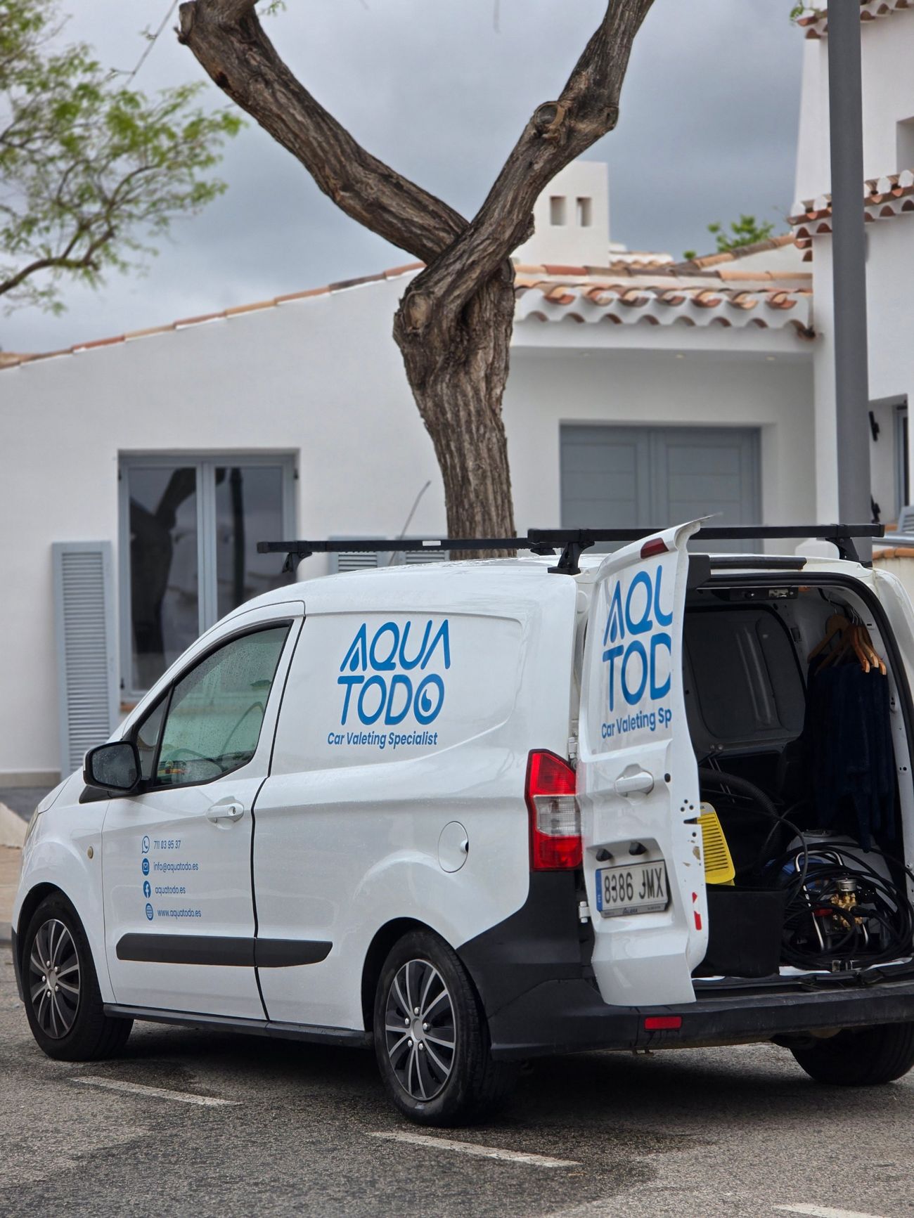 La furgoneta de Aqua Todo frente a una villa blanca, con el portón abierto y el equipo de limpieza dentro
