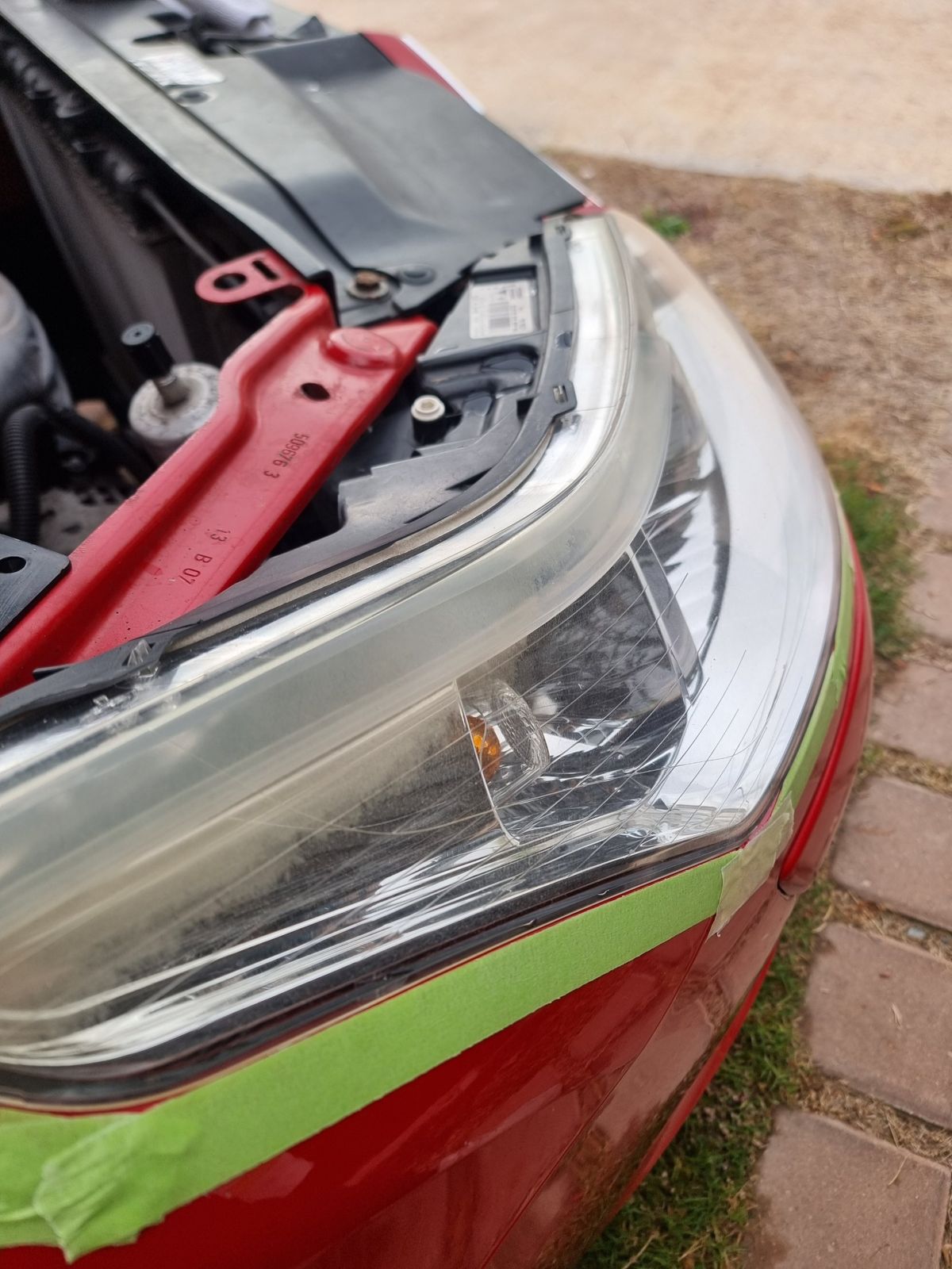 A headlight lens hazed and cracked by years of sun, masked up ready for restoration