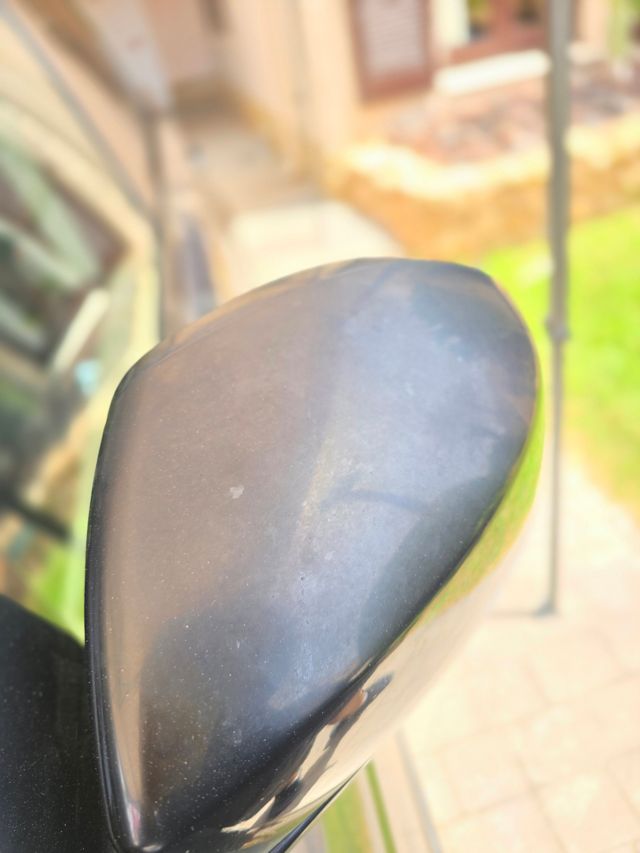 A gloss black wing mirror dulled and faded by the sun